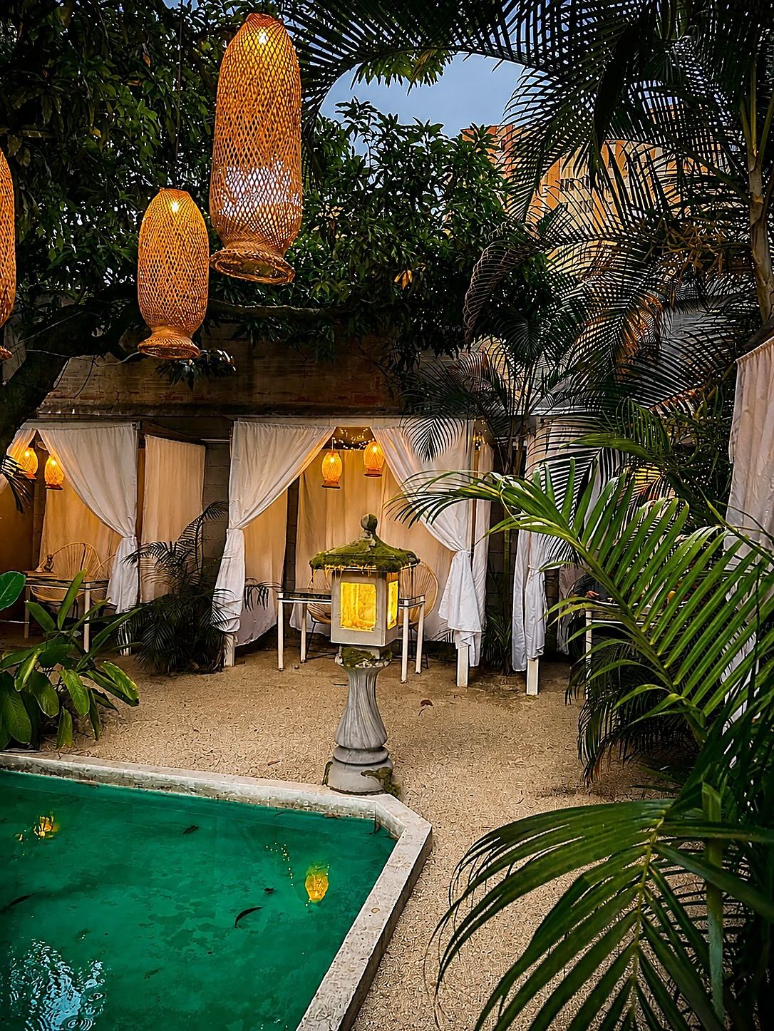 Cabañas con cortinas blancas sobre la arena de Playa Oasis, un farol de piedra encendido y el borde del agua turquesa